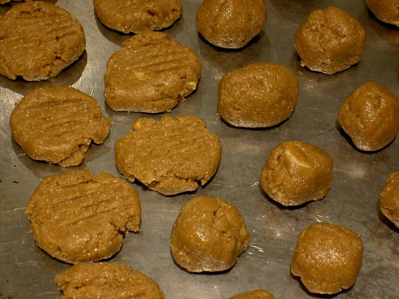 Peanut butter cookies, uncooked on the baking sheet, some flattened by fork